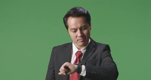An Asian Business Man Checking Watch On Green Screen Background In The Studio