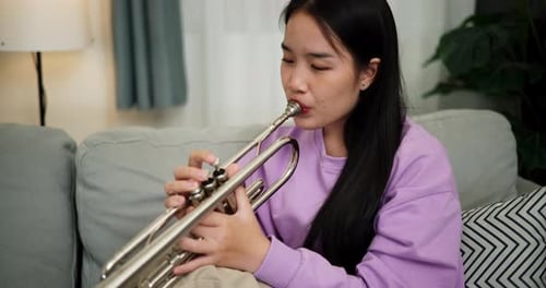 Young Woman Plays Trumpet on Couch Indoors