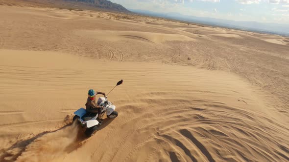 FPV drone shot of an ATV rider riding quads through desert kicking up ...