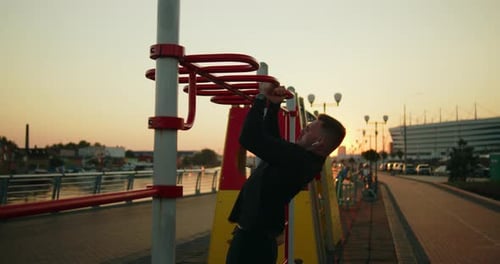 Young Athletic Man Works Out Doing Pullups on a Street Sports Ground at Sunset