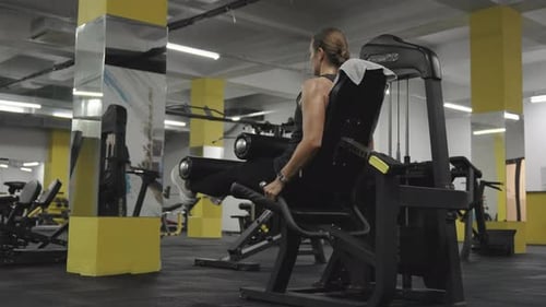 Jovem mulher na frente de um espelho fazendo extensões de pernas em uma máquina. Treinamento e treino esportivo.