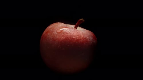 A red apple in drops of water, spinning on a black background, close-up.