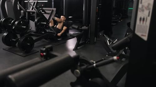 Man Using Leg Press in a Dark Gym