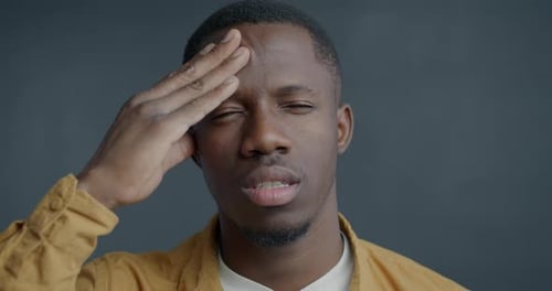 Young Man Holding Forehead in Studio Close Up
