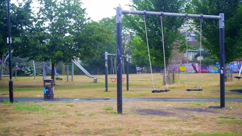 Swing moving slowly in an empty park playground, lockdown emptiness scene