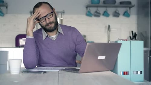 Bearded man working on laptop, getting frustrated, headache