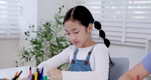 Préadolescente asiatique souriante tout en dessinant en classe à l'aide de crayons de couleur, élève du primaire