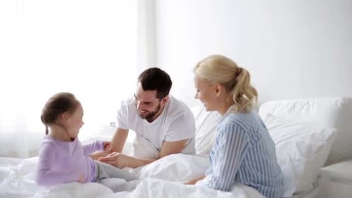 Happy Family Playfully Tickling Child in Bed