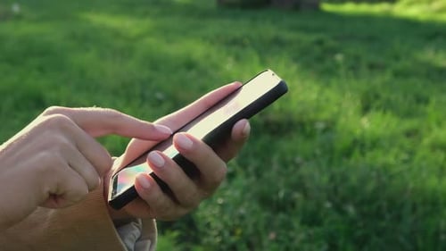 Hands Using Smartphone Outdoors on a Green Background