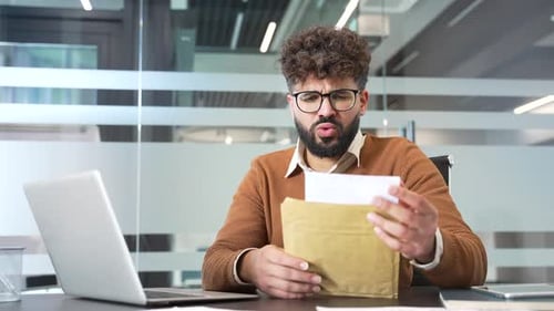 Upset disappointed businessman reading a letter with bad news sitting in business office.