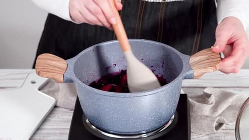 Person stirring simmering blueberry sauce in a pan