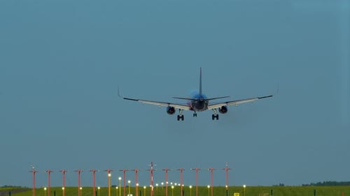 A commercial airplane landing on a runway with navigation lights, green field in the background