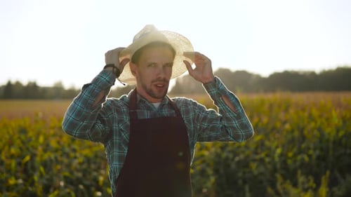 Young Adult Farmer Puts On Straw Hat in Field