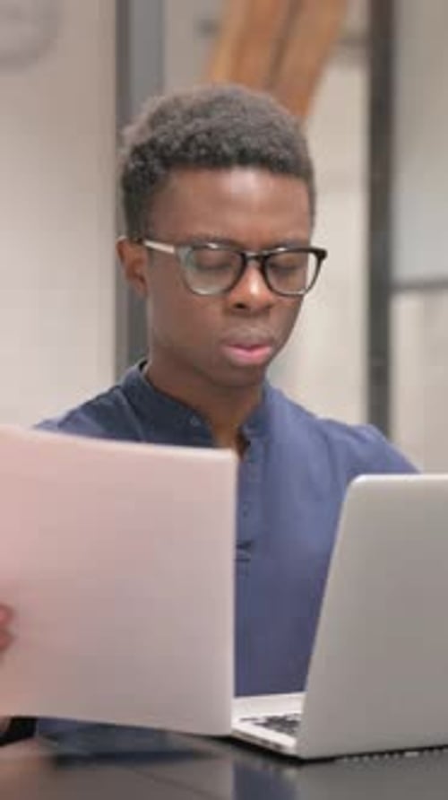 Young Man Reviews Documents at Desk with Laptop