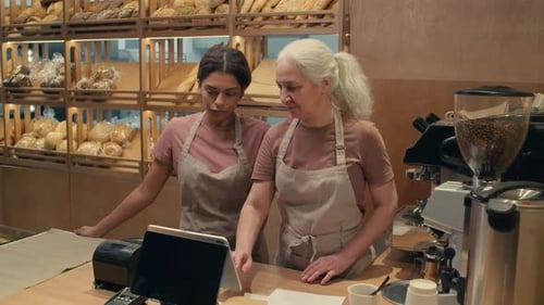 Senior Woman Learning Cash Register with Help of Colleague in Bakery
