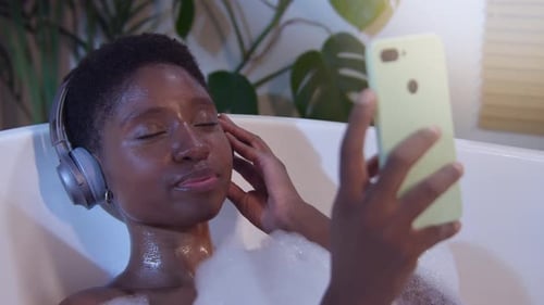Woman Relaxing in Bubble Bath with Headphones and Phone