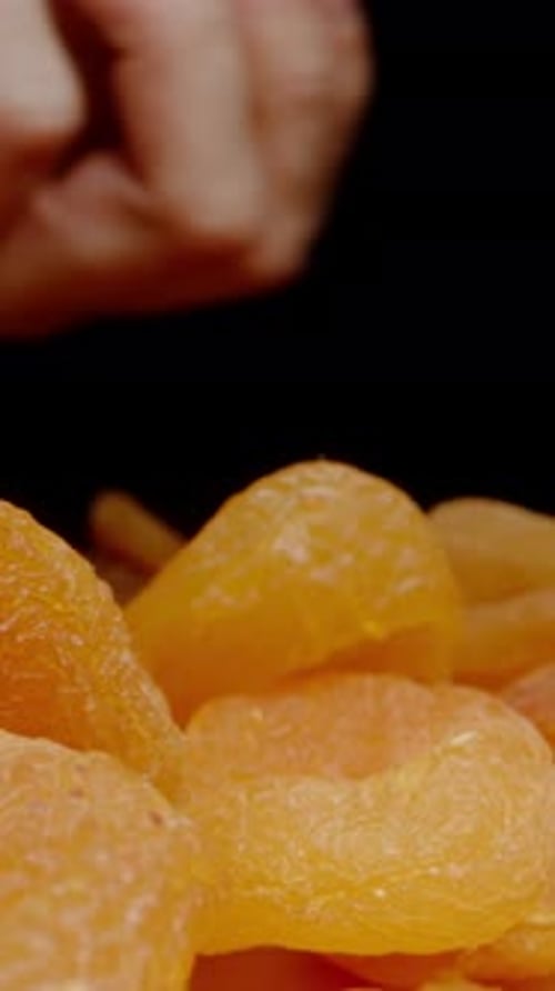 Vertical video. I Pour a Handful of Dried Apricots from the Hand while the Camera Moves Forward.