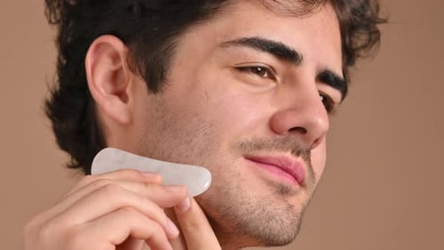 Attractive Man Using Gua Sha Tool For Facial Massage
