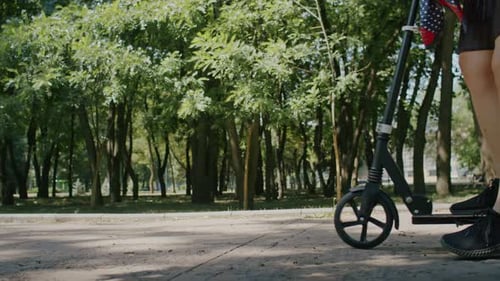 Une fille espiègle profite de l'été et fait du scooter dans les rues du parc et de la ville