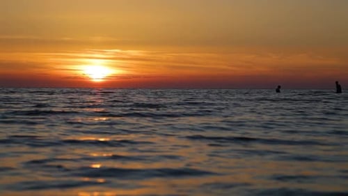 Two guys are swimming in the sea at sunset, faces are not visible, human silhouettes