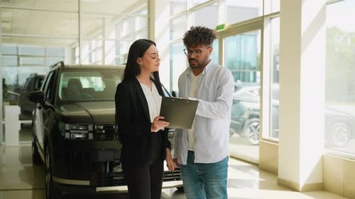 Car Saleswoman Showing Documents to Potential Arabian Buyer in Dealership