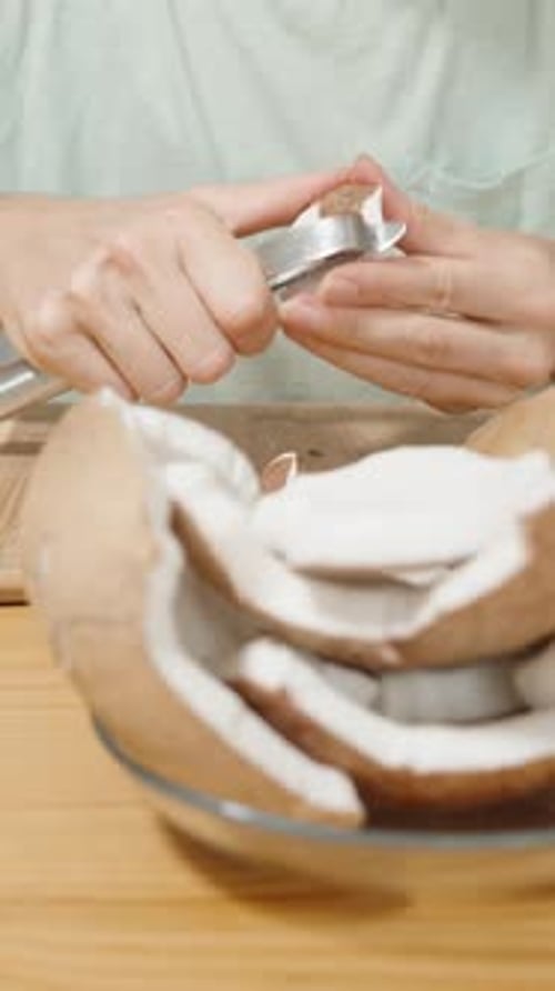 Vertical video. A Woman Peels Coconut Flesh from the Husk Using a Vegetable Knife.