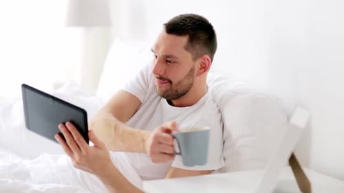 Man in Bed Using Tablet and Drinking Coffee