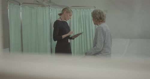 Female Doctor Examining Senior Patient in Hospital, taking notes on Digital Tablet