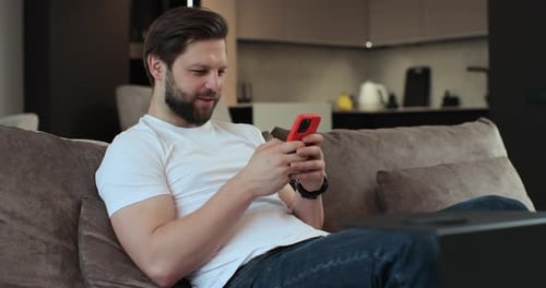 Man Relaxing Using Mobile Phone on Sofa Indoors
