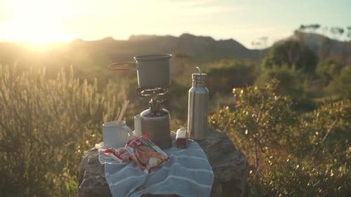 Dolly shot reveals saucepan on portable stove placed on rock at bright campsite in England, UK. The