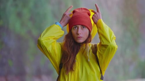 Portrait of a Girl in a Yellow Raincoat Standing Under the Spray of a Waterfall Putting on a Hood to
