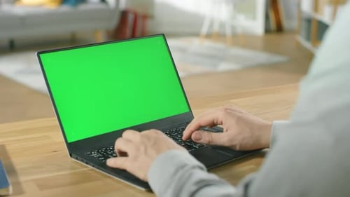 Professional Freelancer Works on a Laptop with Green Mock-up Screen while Sitting at the Desk in Hi