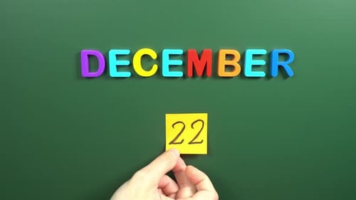 Hand sticking a sticker 22 December calendar day on school board. 22 date of December. Twenty