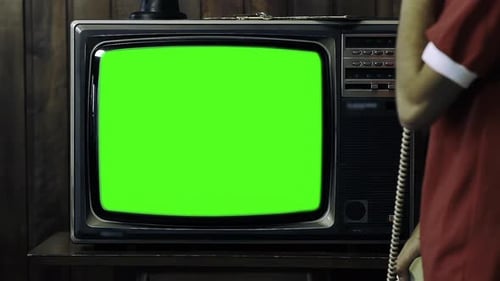 Man Holding 80s Phone While Turning On Old TV with Green Screen in a Dimly Lit Room - 4K