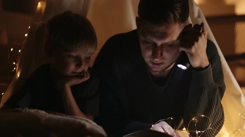 Dad and Son Reading Book in Cozy Tent