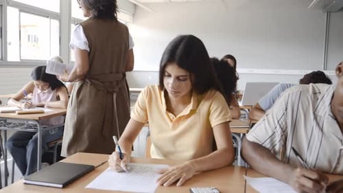 High School Teacher Walking in Class Supervising a Diverse Group of Teens During an Exam