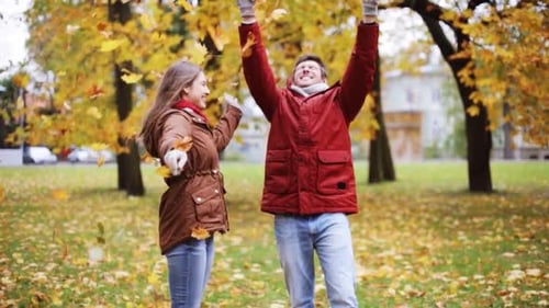 Happy young couple throwing autumn leaves up in park on a romantic fall day