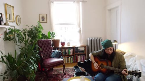 Man with glasses plays guitar in cozy apartment