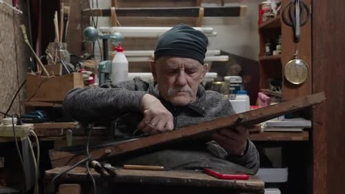 Elderly Male Master Works in His Workshop Restoring Furniture