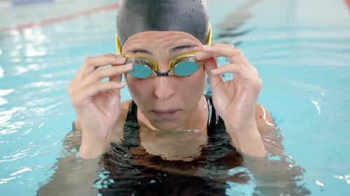 female swimmer adjusting goggles while training in indoor pool, preparing for swim