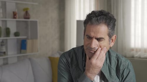 Mature handsome man thinking on sofa in living room.