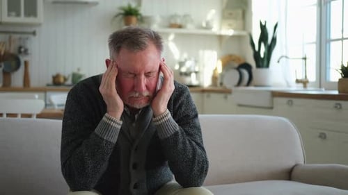 Senior Man Massaging Temples on Couch