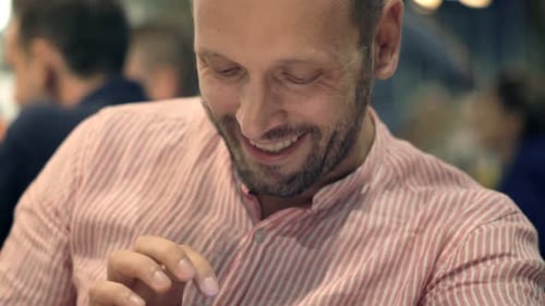 Young Happy Man with Smartwatch Sitting in Cafe at Night 30s