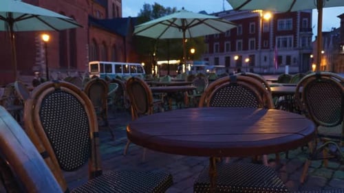 A Serene Evening Setting at an Outdoor Cafe Features Empty Tables Under City Lights Creating a