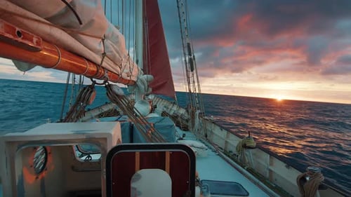 Sailing expedition boat moves in the open sea during bright pink sunrise