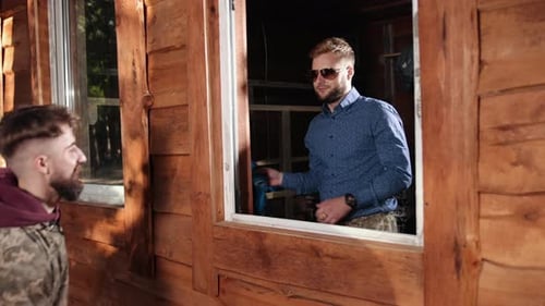 Two Young Men Pass an Object Through Window