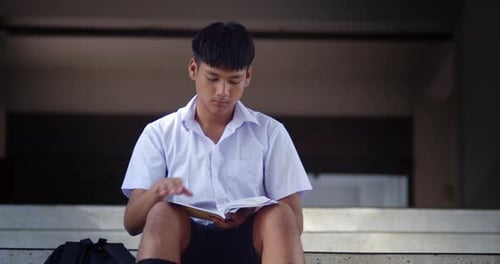 A male high school student in a white school uniform is sitting and studying alone
