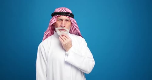 Senior man in traditional dress talking on blue background