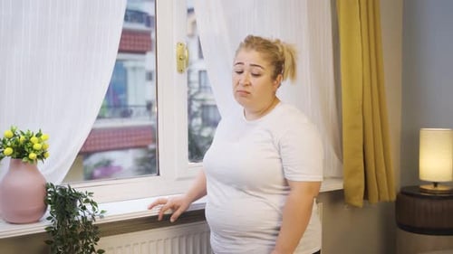 Adipositas Frau schaut unglücklich vor dem Fenster raus.