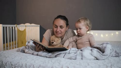 Mother Reads Book to Baby in Bed